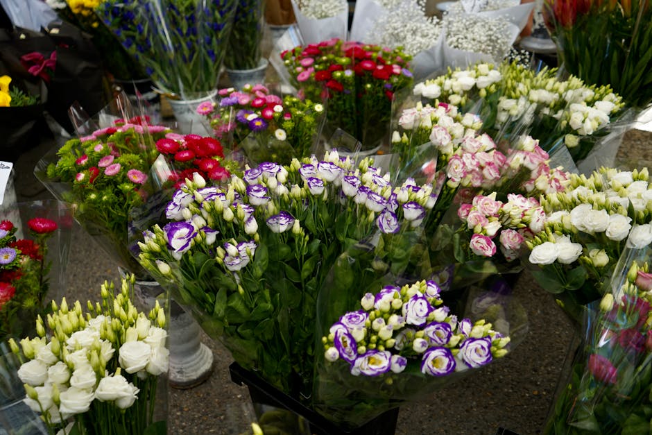A variety of freshly cut flowers arranged in bouquets and displayed on a table at a florist shop. The floral selection includes purple and white eustoma, pink and white roses, red gerbera daisies, whi
