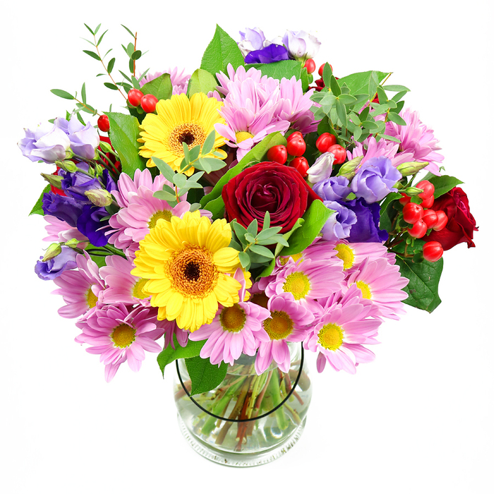 A colourful mixed bouquet rises confidently from a clear glass vase, its rounded shape and dense cluster of blooms captured against a bright white backdrop. In the centre, deep red roses form a strong, romantic heart, their velvety petals layered so that each flower seems to glow from within. Nestled nearby are two radiant yellow gerbera daisies, their broad petals surrounding dark brown-orange centres that add friendly, almost smiling faces to the design. Around these key flowers, generous sprays of pink and lilac daisies or chrysanthemums spill outward, their delicate, multi-petalled heads and tiny yellow centres adding both volume and softness, much like the gentle, blooming borders found in Cranford's gardens in late spring. Purple and lavender lisianthus stems weave gracefully through the arrangement, some blossoms fully open, others held in tapered buds, giving the bouquet height and a sense of motion, as if a light breeze were rustling the petals. Interspersed between the flowers are clusters of bright red hypericum berries, their smooth, rounded forms catching the light and adding an appealing, tactile contrast. Lush green foliage frames the entire composition; broad, deep green leaves offer sturdy shapes and shadows, while slender, paler green sprigs add brightness and a hint of wildness. The clear glass vase below reveals well-trimmed stems fanned neatly in the water, a quiet testament to professional craftsmanship and balance. This arrangement feels ideal for sitting on a dining table in a Cranford family home, welcoming guests in a hallway near Cranford Park, or arriving as a same-day delivery to celebrate a birthday, promotion, or new chapter with a vivid and uplifting burst of colour.